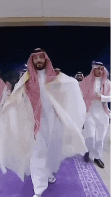 a man in a white robe and a red scarf is walking on a purple carpet .