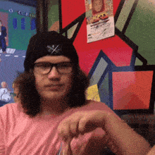 a young man wearing glasses and a black hat with a cross on it looks at the camera
