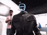 a man is standing next to a mannequin wearing a leather jacket and helmet .