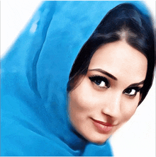 a woman wearing a blue scarf on her head looks at the camera