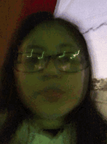 a woman wearing glasses looks at the camera with a green background