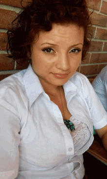 a woman in a white shirt is taking a selfie with a brick wall in the background