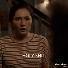 a woman in a striped shirt says holy shit in front of a staircase