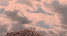 a squirrel standing on top of a rock with a cloudy sky behind it