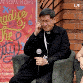 a priest is sitting in front of a sign that says " radice "