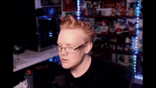 a man wearing glasses is sitting in front of a microphone in a room filled with toys .