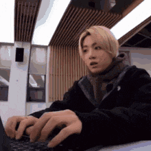 a man is typing on a laptop computer while wearing a black jacket and scarf .