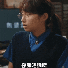 a woman wearing glasses and a blue vest has chinese writing on her shirt