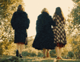 three women in coats are walking in the grass