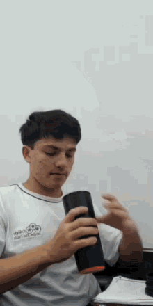 a young man wearing a shirt that says ' angels ' on it is holding a black cup