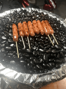 a bunch of sausages on sticks are sitting on a pile of black beans