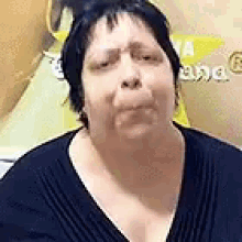 a woman in a black sweater is making a funny face in front of a yellow wall .