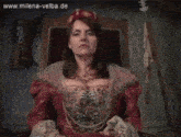 a woman in a red dress sits in a chair with the website www.milena-velba.de visible