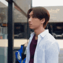 a young man wearing a white shirt and a maroon shirt is standing in front of a building .
