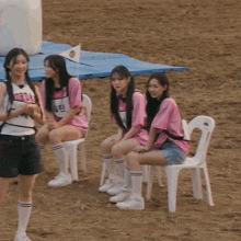 a group of girls are sitting on chairs in the dirt .