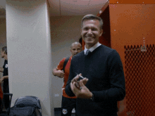 a man in a black sweater is smiling in front of an orange locker