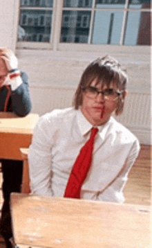 a man wearing glasses and a red tie is sitting at a desk .