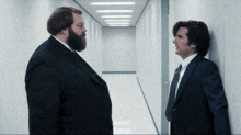 two men in suits and ties are standing in a hallway