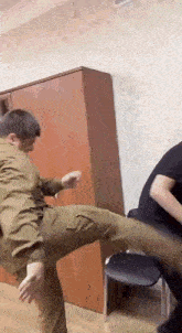 a man in a military uniform is kicking another man in the leg in a room .
