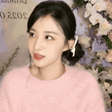 a woman wearing a pink sweater is standing in front of flowers and a sign that says 50520