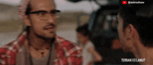 a man wearing glasses is talking to another man in a video that says terbaik