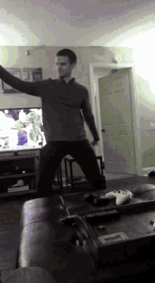 a man is dancing in front of a tv in a living room with a playstation controller on the table
