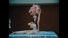 a woman is sitting on a bed wearing a feathered hat