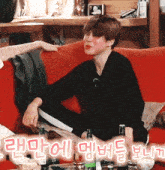 a man sits on a red couch with bottles of beer in front of him in korean writing