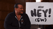a man sitting in front of a sign that says hey ew