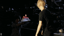 a man holding a cake on a stage with the letter d on the bottom