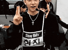 a young man wearing a black sweater and a white apron is giving a peace sign .