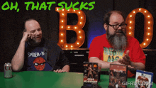two men are sitting at a table with a sign that says oh that sucks