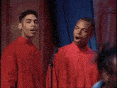 a group of men singing into microphones with one wearing sunglasses and a blue shirt