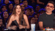 a woman stands in front of a microphone while a man sits behind her with nbc written on the bottom