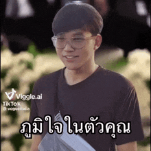 a young man wearing glasses and a black t-shirt is smiling and holding a book .