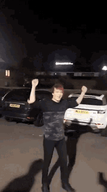 a man is dancing in a parking lot with his arms in the air in front of a range rover .