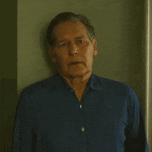 a man in a blue shirt is leaning against a green wall with his eyes closed