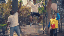 a group of men are jumping in the air while holding balloons in a park .
