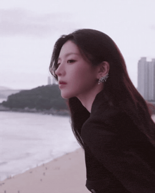 a woman in a black jacket stands on a beach