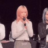 a woman with pink hair is holding a microphone in front of a crowd .