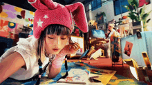 a girl wearing a pink bunny hat is laying on the floor drawing in a notebook .