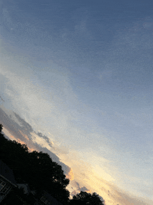 a sunset sky with trees in the foreground and a house in the background