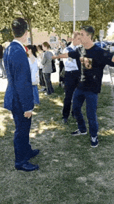a man in a suit and a man in a black shirt are standing in a grassy field