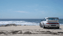 a white porsche 911 is parked on a beach