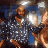 a man in a floral shirt is dancing in front of a sign that says friday rises