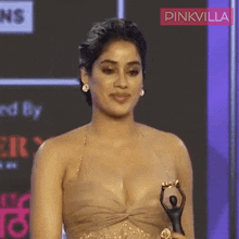 a woman in a very plunging dress is holding a trophy in front of a pinkvilla logo