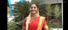 a woman in a red and gold saree with flowers in her hair is smiling .