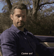 a man in a purple shirt is sitting in a car and says come on