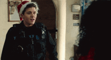 a police officer wearing a santa hat talks to a lady