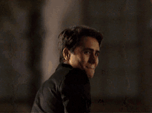 a man in a black suit is smiling and looking over his shoulder